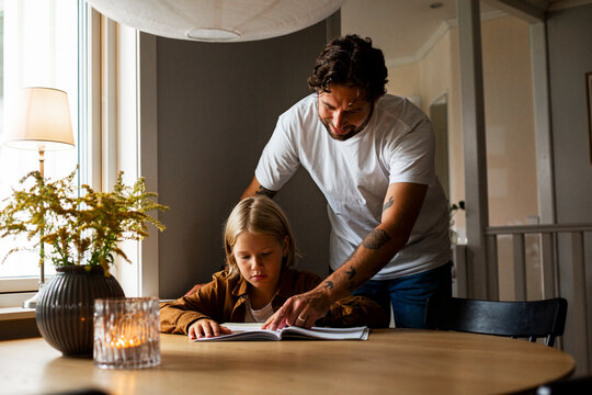 Smiling man helping son with homework sitting at table