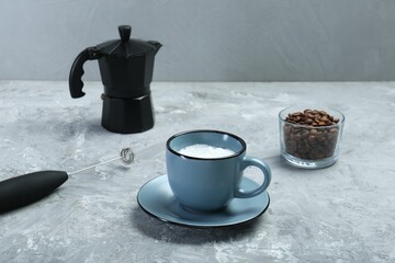 Mini mixer (milk frother), whipped milk in cup and coffee beans on grey textured table