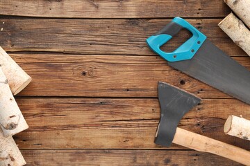 Saw with light blue handle, axe and firewood on wooden background, flat lay. Space for text