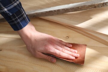 Man polishing wooden planks with sandpaper, closeup