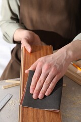 Man polishing wooden plank with sandpaper at grey table, closeup