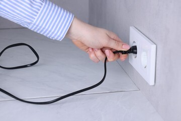 Woman inserting electric plug into socket at white table indoors, closeup