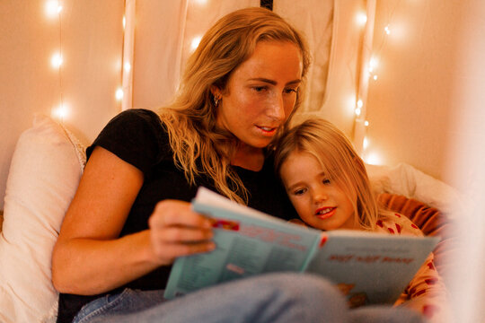 Mother and daughter reading picture book in bedroom at home