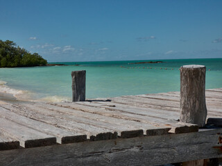 Wooden pier on a paradisiacal and lonely beach with a blue sky on the horizon