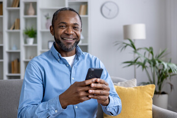 A relaxed man in a blue shirt at home, engaging with his smartphone, surrounded by modern decor.