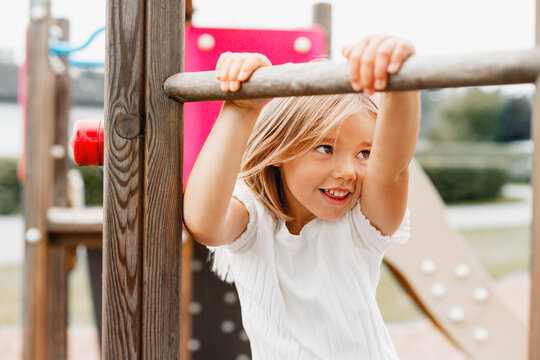 Cute smiling blond girl playing on jungle gym in playground