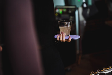 Person holding a glass of liquid on a tray at an event