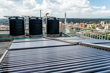 Water tank on the roof over blue sky. Black water tank on the roof of a tall building against a blue sky. water heating system on the roof of a high-rise building in southern countries.