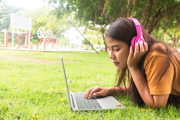 Girl enjoy listening music and reading a book and play laptop on the grass field of the park in the morning