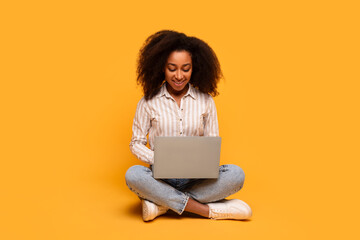 Woman sitting with laptop on floor on yellow background
