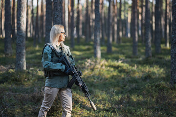 Beautiful army girl with a modern AK 12 suppressed rifle in the forest at war.