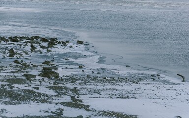 Closeup shot of a rocky shore with stones and a frozen lake before it on a cold winter day