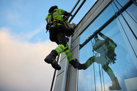 Low angle view of rope access worker hanging on glass building