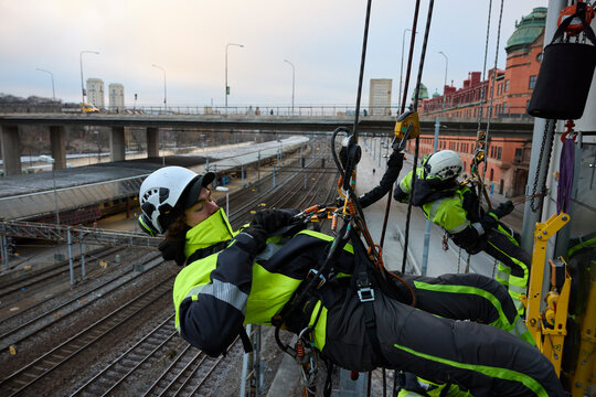 Rope access worker fastening carabiner to rope while hanging from building
