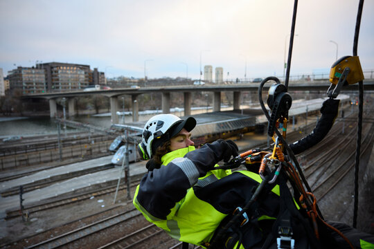 Rope access worker fastening carabiner to rope while hanging over railroad tracks