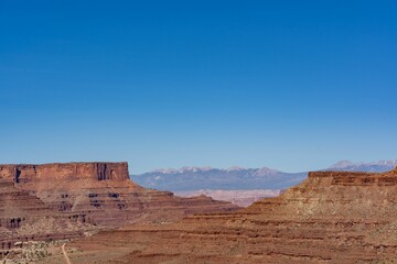 Peaceful desert landscape in a canyon with dry brown fields and rocky cliffs under a clear blue sky