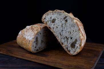 A loaf of designer bread cut in half with seeds on a wooden board. Art bread.