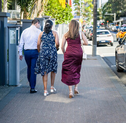 Three young people walking on the pedestrian footpath along a busy street. Takapuna. Auckland.