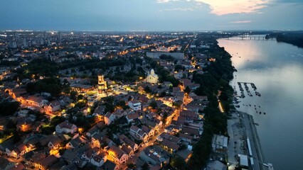Aerial shot of the illuminated Zemun village and Belgrade next to the Sava river in the evening - obrazy, fototapety, plakaty