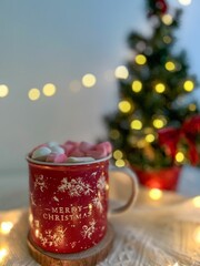 Christmas mug full of marshmallows with a Christmas tree on the blurred background