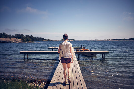 Full length rear view of woman walking on jetty over lake during sunny day