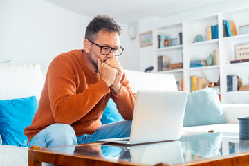 Focused adult Caucasian man in glasses sit on sofa at home work online on laptop gadget....