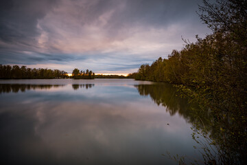 Beautiful sunset over the lake surrounded by trees which reflect in the water in Bavaria, Germany
