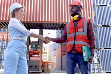 Two worker wearing safety helmet shaking hands at logistic shipping cargo containers yard. African...