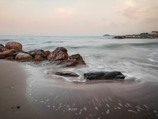 Foamy sea waves hitting a beach with stones leaving its traces on the sand