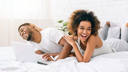 Young black couple lying on bed and using laptop.