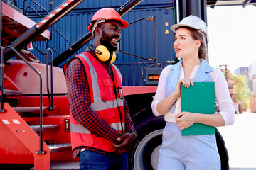 Two workers with safety helmet at logistic shipping cargo containers yard. African American engineer man discuss results with his beautiful woman boss who holds document folder at workplace.