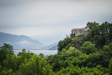 Green nature with tre near a harbor in Maggiore lake under a cloudy sky, Lombardy, Italy - obrazy, fototapety, plakaty