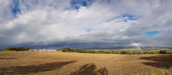 Panoramic view of a cultivated field with a rainbow under a cloudy sky