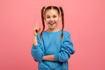 Girl pointing upwards with a smile on pink background