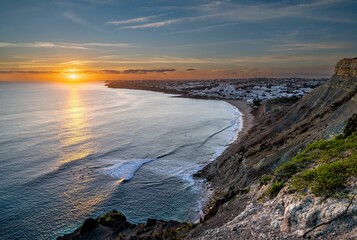 Scene of the ocean with the rocky beach illuminated by sun rays at sunset in Praia da Luz, Portugal