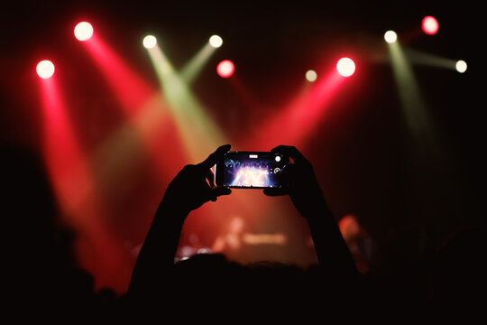 Holding a phone and taking photos of the concert. Concert background.
