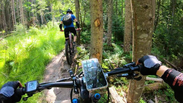 Point of view. Couple of cyclist riding electric mountain bikes in the forest. Smartphone on bicycle handlebar. Concept of adventure, leisure time outdoors.