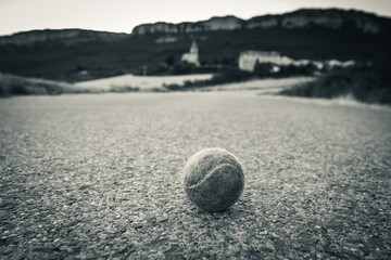 closeup of isolated tennis ball sitting on an empty road, black and white