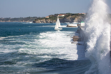 splashing wave against the dike and a sailing boat in Socoa, basque country