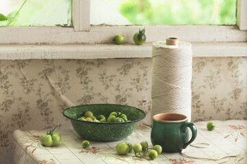 Cottage window and kitchen with old dishes, a skein of rope and green tomatoes on the table