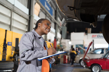 Female mechanic working at garage. Female mechanics checking car engine underneath lifted car at auto car repair service. Car service and Maintenance concept - obrazy, fototapety, plakaty