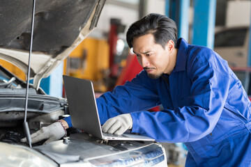 Male mechanic working at garage. Asian male mechanics using laptop computer checks, repair and...