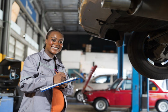 Female mechanic working at garage. Female mechanics checking car engine underneath lifted car at auto car repair service. Car service and Maintenance concept