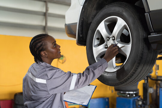 Female mechanic working at garage. Female mechanics checking tire wheel underneath lifted car at auto car repair service. Car service and Maintenance concept