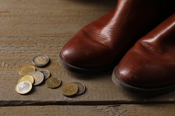 Poverty. Old boots and coins on wooden table, closeup - obrazy, fototapety, plakaty