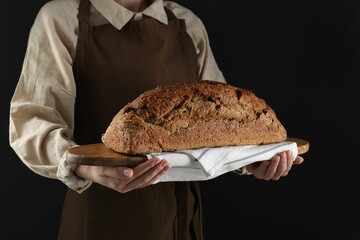 Woman holding freshly baked bread on black background, closeup