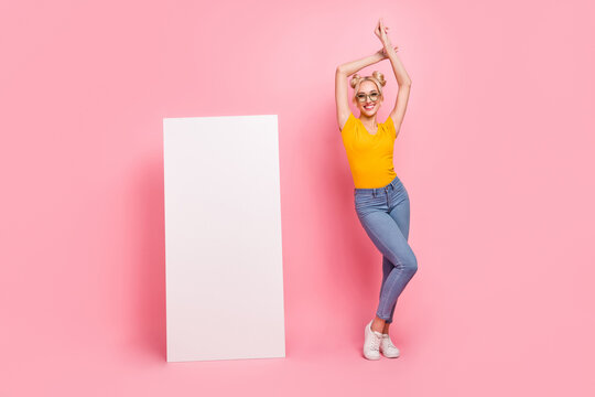 Full length photo of cute blond lady dance near advert wear eyewear t-shirt jeans shoes isolated on pink background
