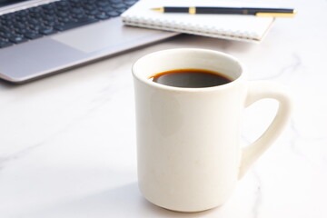 コーヒーを飲みながらノートパソコンでデスクワークをしているイメージ