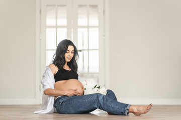 Pregnant woman sitting on floor holding bouquet of flowers