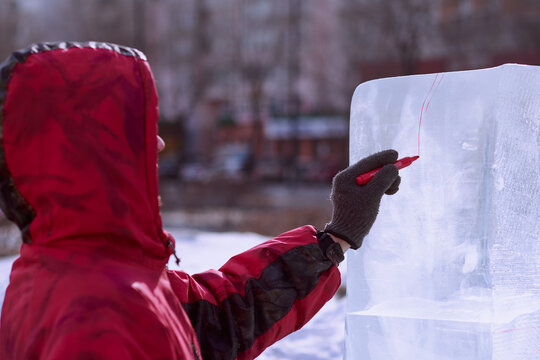 A sculptor draws a red line on an ice block. Preparing to create a sculpture at the city winter festival of artistic ice figures.